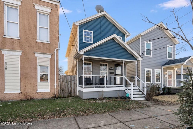 view of front of property with covered porch, a front lawn, fence, and brick siding