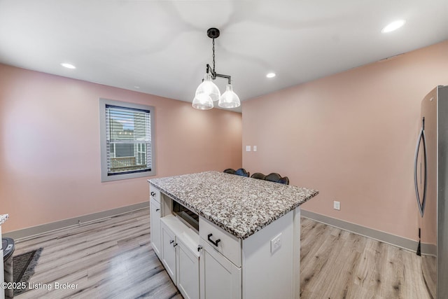 kitchen with baseboards, light stone counters, freestanding refrigerator, and light wood-style floors