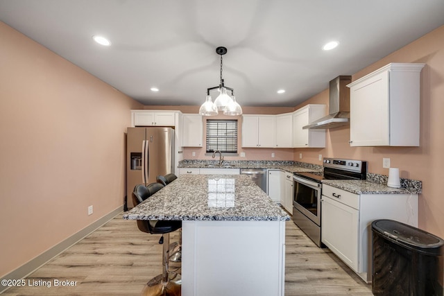 kitchen featuring light wood-style flooring, stainless steel appliances, a sink, wall chimney range hood, and a center island