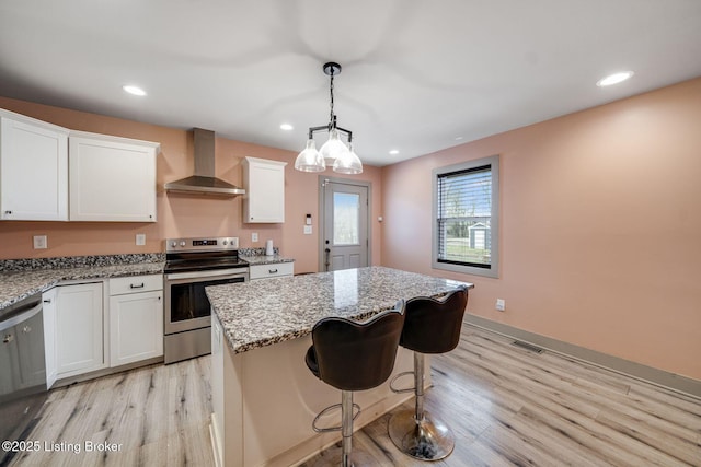 kitchen with light stone counters, light wood-style floors, a kitchen island, stainless steel range with electric stovetop, and wall chimney exhaust hood