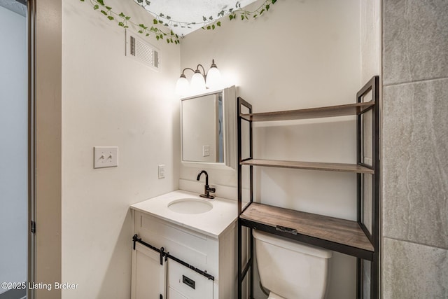 bathroom featuring toilet, vanity, and visible vents