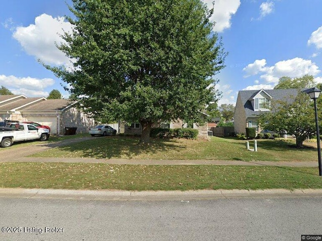 view of property hidden behind natural elements featuring driveway, a front lawn, an attached garage, and a residential view