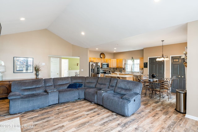 living area with high vaulted ceiling, light wood finished floors, recessed lighting, and an inviting chandelier