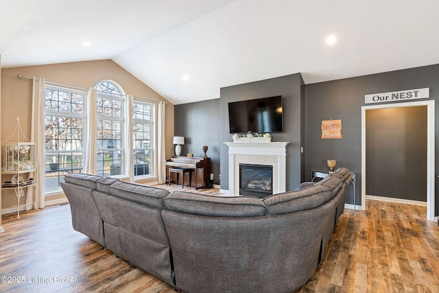 living area with lofted ceiling, baseboards, wood finished floors, and a glass covered fireplace