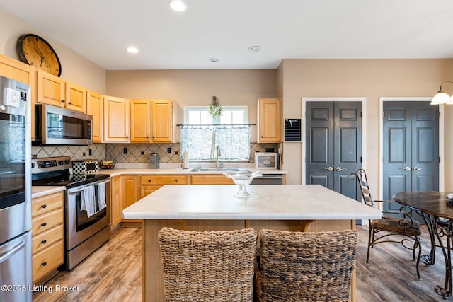 kitchen with appliances with stainless steel finishes, a center island, light countertops, and light brown cabinets