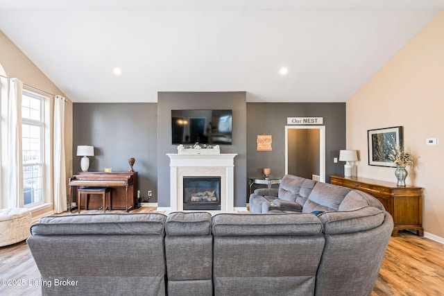 living room with light wood-style floors, a glass covered fireplace, vaulted ceiling, and baseboards