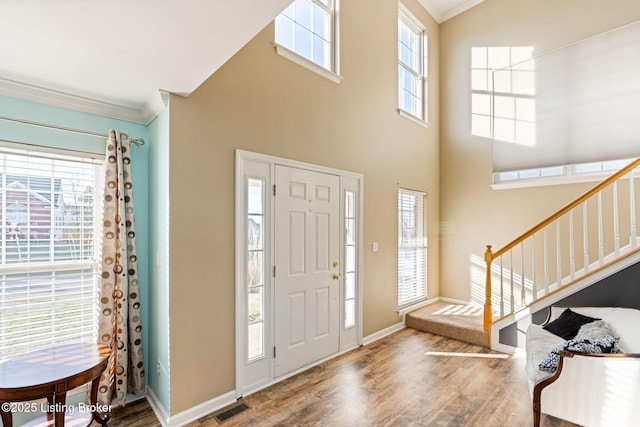 foyer featuring visible vents, ornamental molding, a healthy amount of sunlight, wood finished floors, and stairs