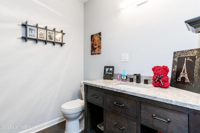 half bath featuring baseboards, vanity, toilet, and wood finished floors