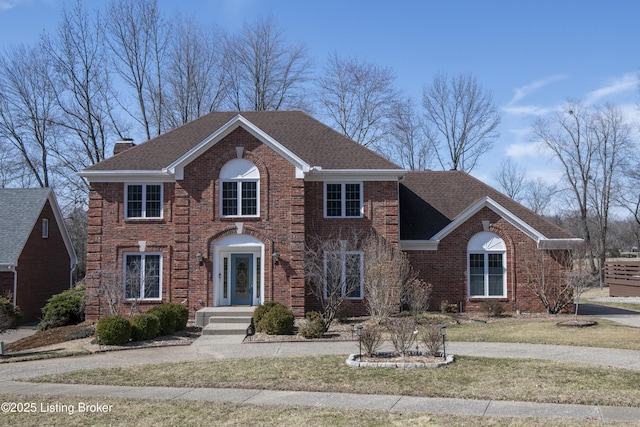 view of front of property featuring brick siding, a chimney, a front lawn, and roof with shingles