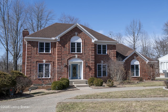 colonial home with brick siding, a chimney, and a shingled roof