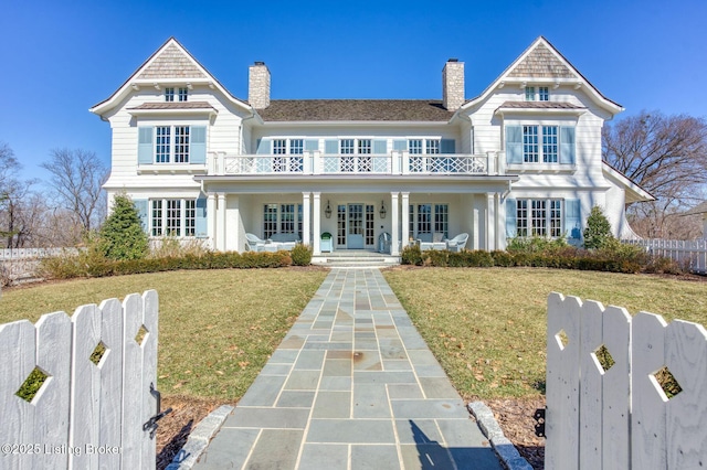 view of front facade with covered porch, a front yard, fence, and a balcony