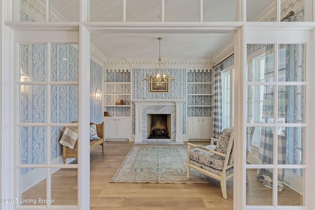 sitting room featuring a high end fireplace, a notable chandelier, crown molding, and wood finished floors