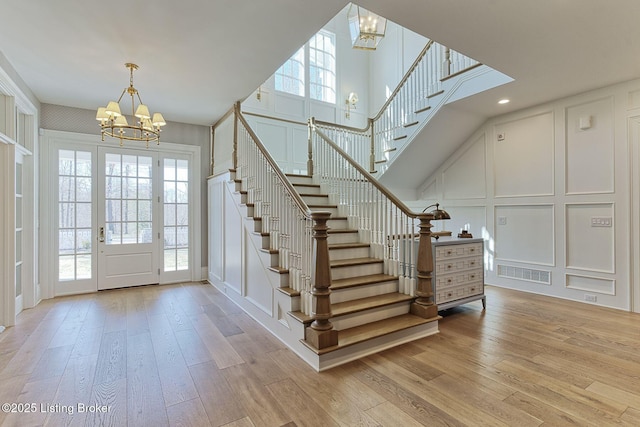 foyer featuring stairway, a notable chandelier, a decorative wall, and light wood-style flooring