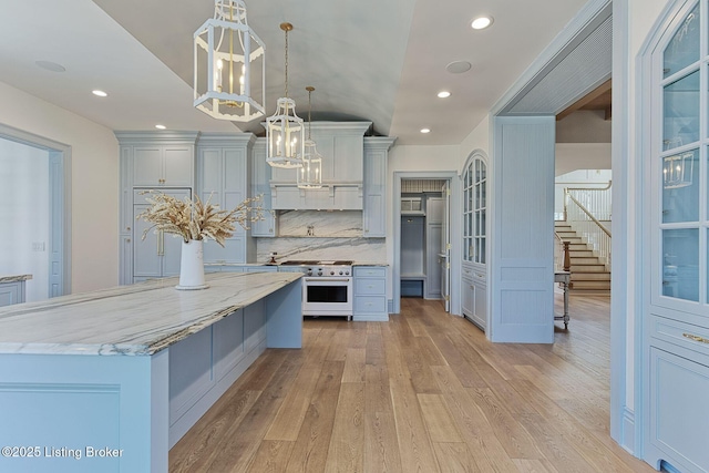 kitchen with light stone counters, pendant lighting, range with gas cooktop, light wood finished floors, and backsplash