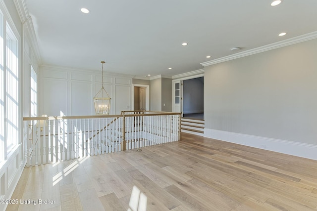 spare room featuring plenty of natural light, crown molding, light wood finished floors, and an inviting chandelier