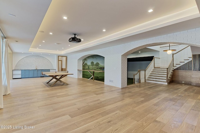 interior space featuring recessed lighting, a raised ceiling, stairway, light wood-style flooring, and brick wall