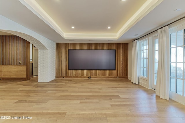 cinema featuring arched walkways, a raised ceiling, light wood-style flooring, and recessed lighting