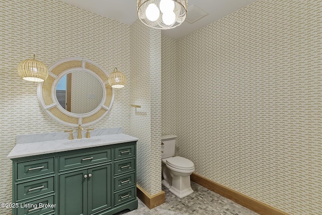 bathroom with toilet, wallpapered walls, baseboards, and vanity