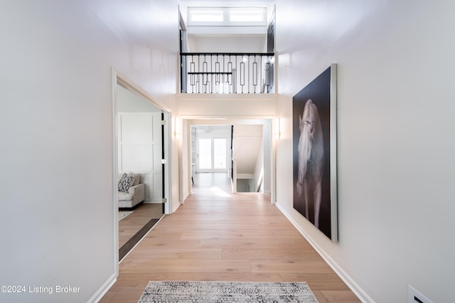 hall with a towering ceiling, light wood-style flooring, and baseboards