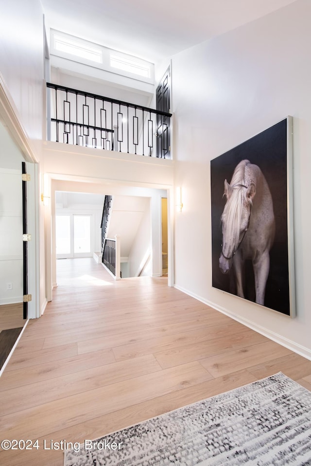 corridor featuring a towering ceiling, baseboards, wood finished floors, and an upstairs landing