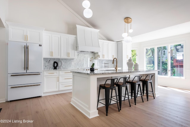 kitchen featuring premium range hood, a kitchen island with sink, white cabinets, and high end fridge