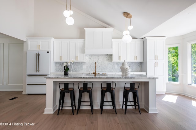 kitchen featuring high end white refrigerator, a center island with sink, white cabinetry, and light stone countertops