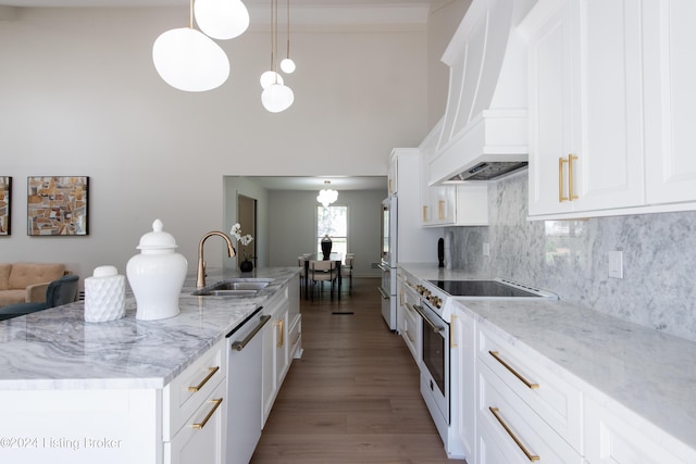 kitchen with white appliances, decorative light fixtures, premium range hood, white cabinetry, and a sink