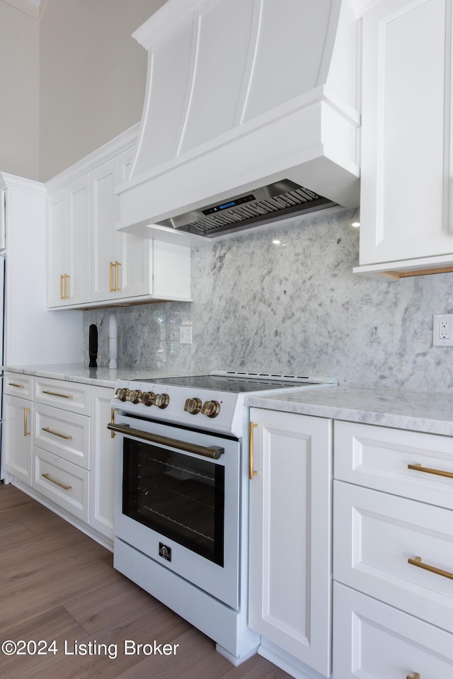 kitchen featuring white range with electric stovetop, white cabinets, premium range hood, and backsplash