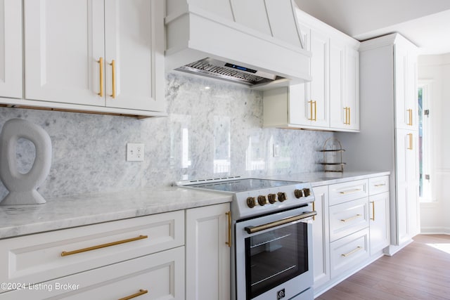 kitchen featuring light stone counters, premium range hood, high end white range, white cabinets, and backsplash