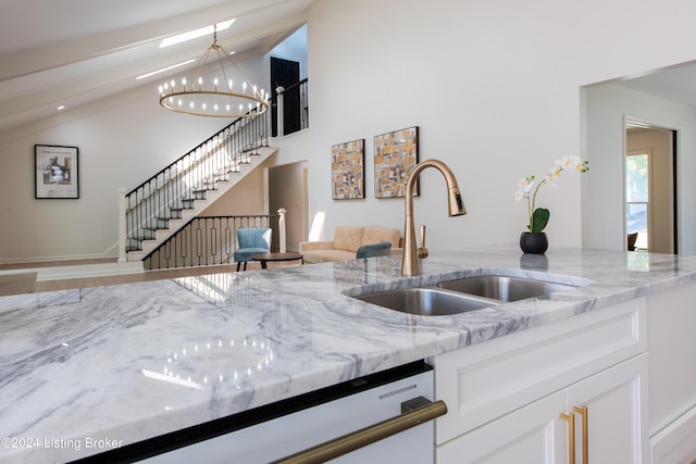 kitchen with high vaulted ceiling, a notable chandelier, a sink, white cabinets, and light stone countertops