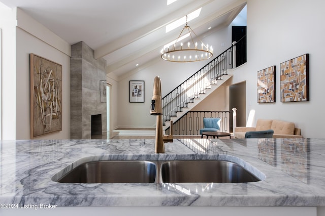 kitchen with a notable chandelier, a tiled fireplace, a sink, light stone countertops, and beamed ceiling