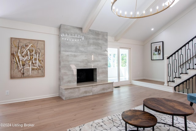 living room with vaulted ceiling with beams, a premium fireplace, stairway, light wood-type flooring, and an inviting chandelier