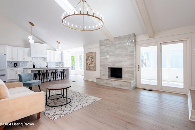 living room featuring a chandelier, beamed ceiling, a fireplace, and light wood-style flooring