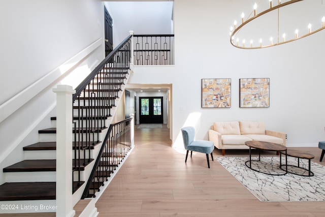 interior space featuring a towering ceiling, stairway, french doors, light wood-style floors, and a chandelier