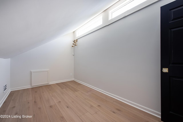 additional living space featuring light wood finished floors, baseboards, and vaulted ceiling