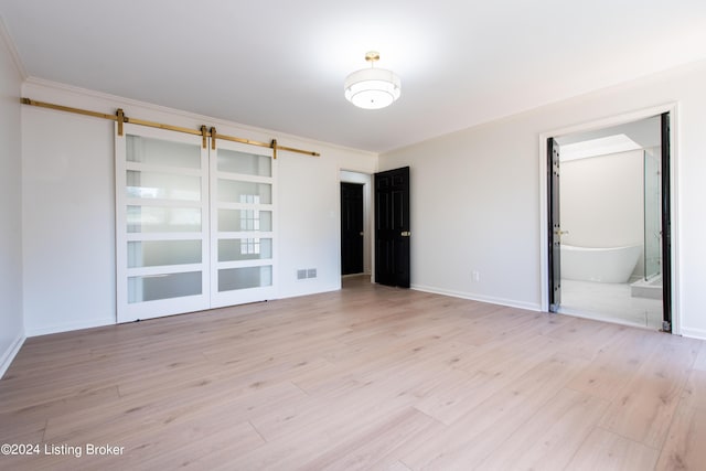 unfurnished room with a barn door, visible vents, baseboards, crown molding, and light wood-type flooring