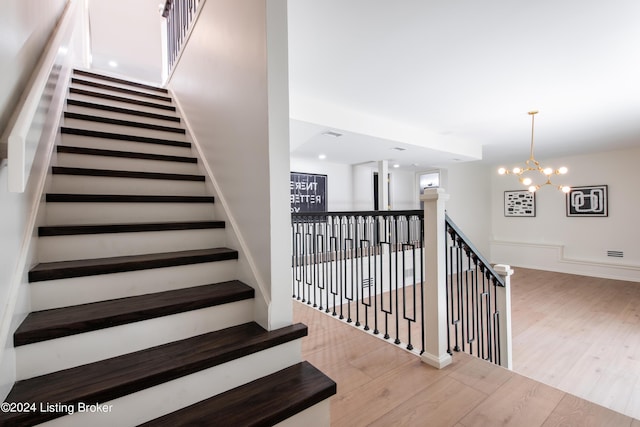 stairs with baseboards, wood finished floors, visible vents, and an inviting chandelier