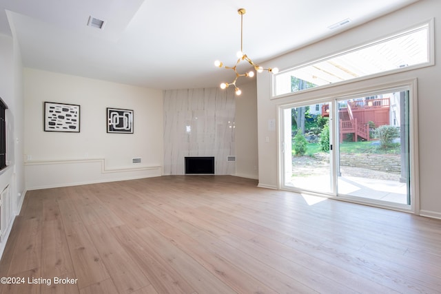 unfurnished living room with a large fireplace, a notable chandelier, visible vents, and light wood-style floors