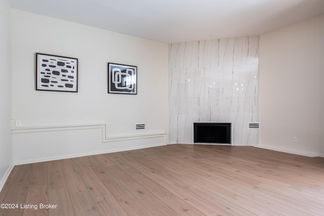 unfurnished living room with light wood-type flooring, a premium fireplace, and baseboards