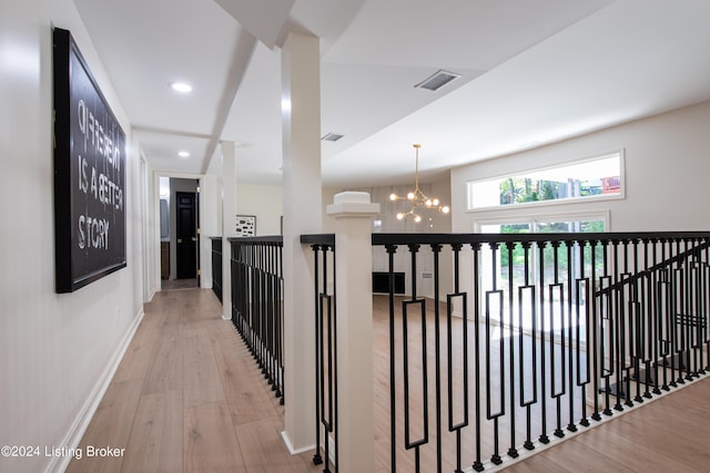 corridor featuring light wood finished floors, baseboards, visible vents, an upstairs landing, and a notable chandelier