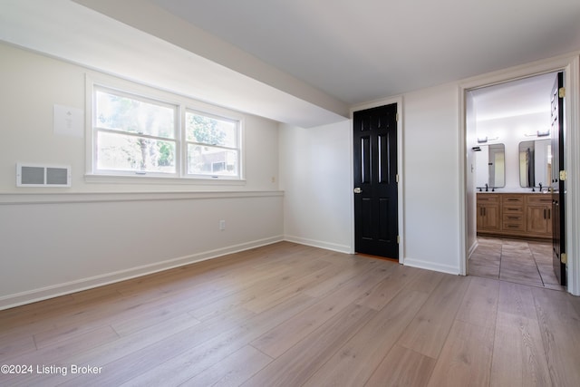 unfurnished bedroom with light wood finished floors, baseboards, visible vents, ensuite bath, and a sink