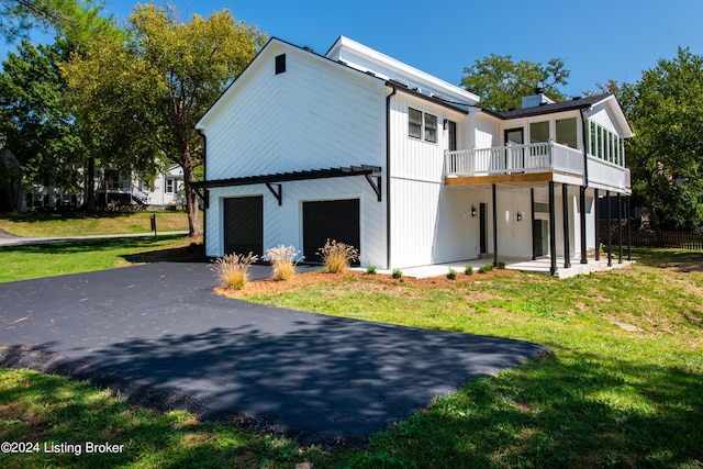 view of side of home with a yard, an attached garage, a balcony, and driveway