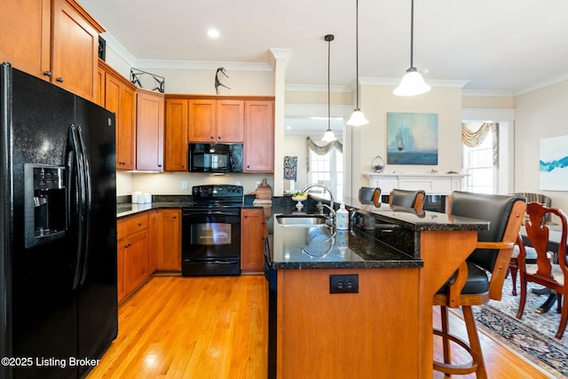 kitchen featuring a breakfast bar area, decorative light fixtures, a kitchen island with sink, black appliances, and a sink