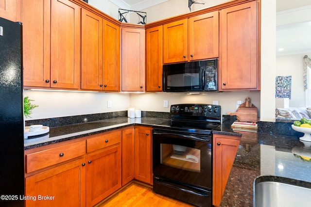 kitchen featuring light wood-type flooring, black appliances, brown cabinets, and dark stone counters