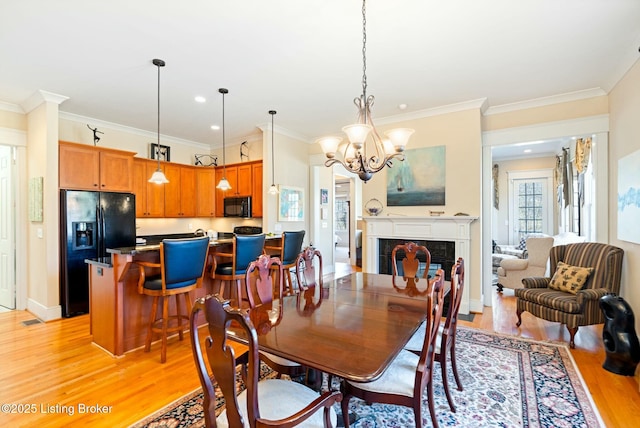 dining space featuring light wood-style floors, a chandelier, crown molding, and a tile fireplace