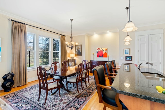 dining area with light wood-style flooring, ornamental molding, and a notable chandelier