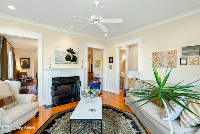 living room featuring baseboards, a ceiling fan, ornamental molding, wood finished floors, and a fireplace