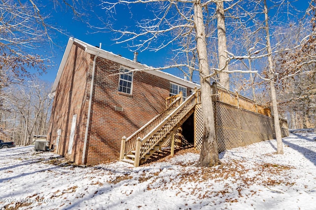 view of snowy exterior with central AC, brick siding, and stairway