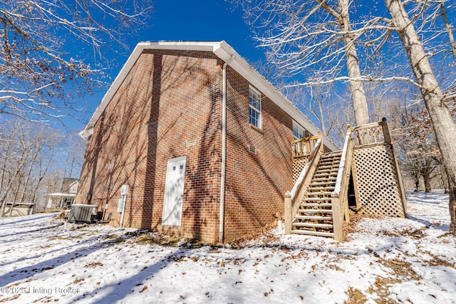 view of snowy exterior with central air condition unit, stairway, and brick siding