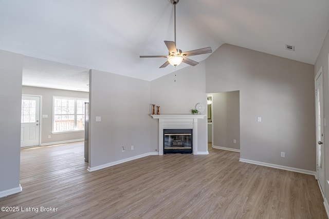 unfurnished living room featuring light wood-style flooring, visible vents, baseboards, and a glass covered fireplace